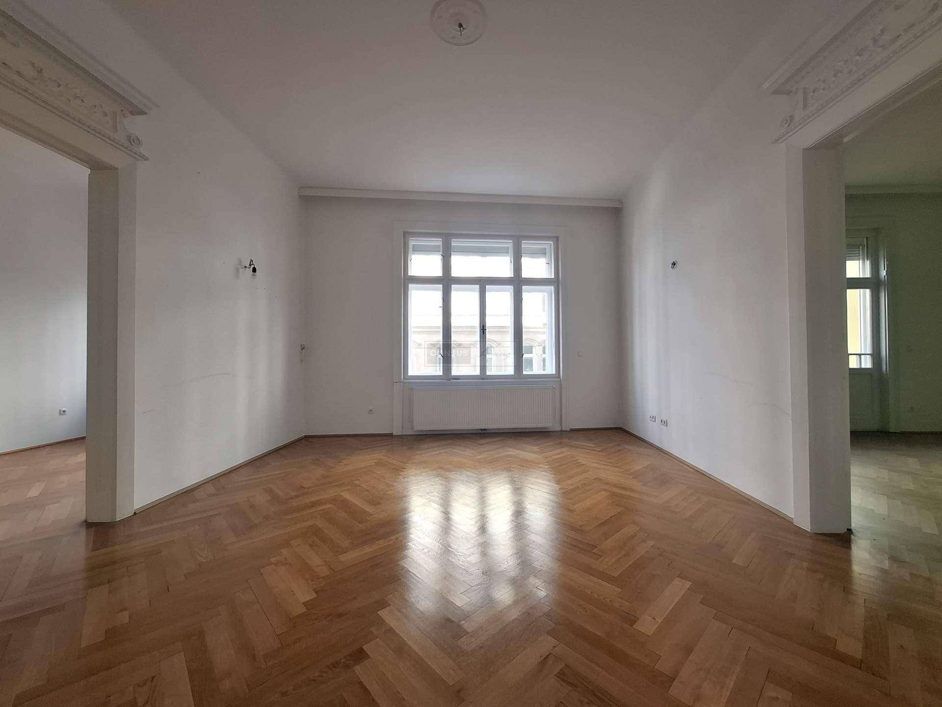 Helles, leeres Zimmer mit klassischem Fischgrätparkett und großen Fenstern, bereit zur Gestaltung.