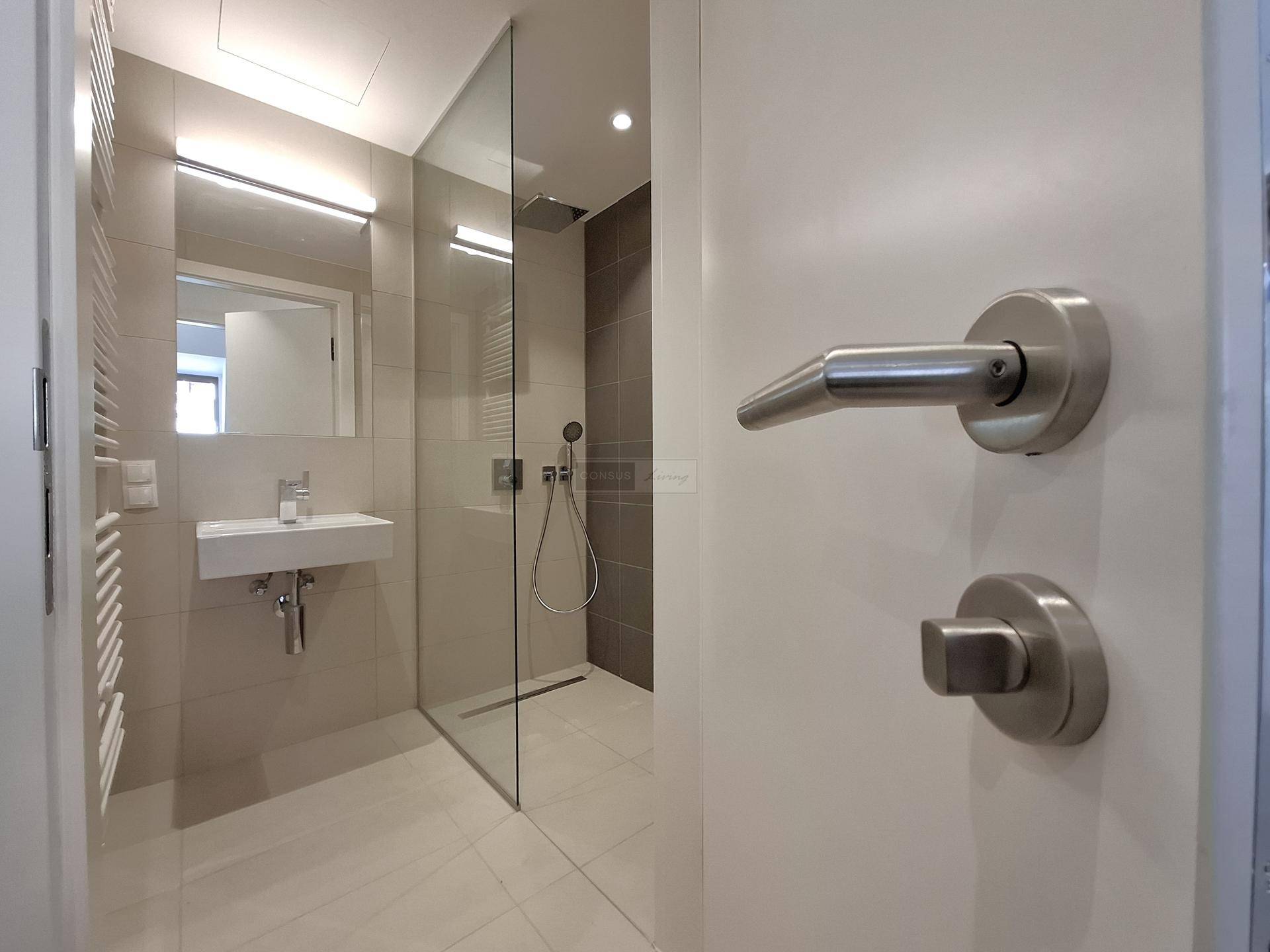 Elegantes Badezimmer mit großer Glasdusche, modernem Waschtisch und hellen Fliesen.