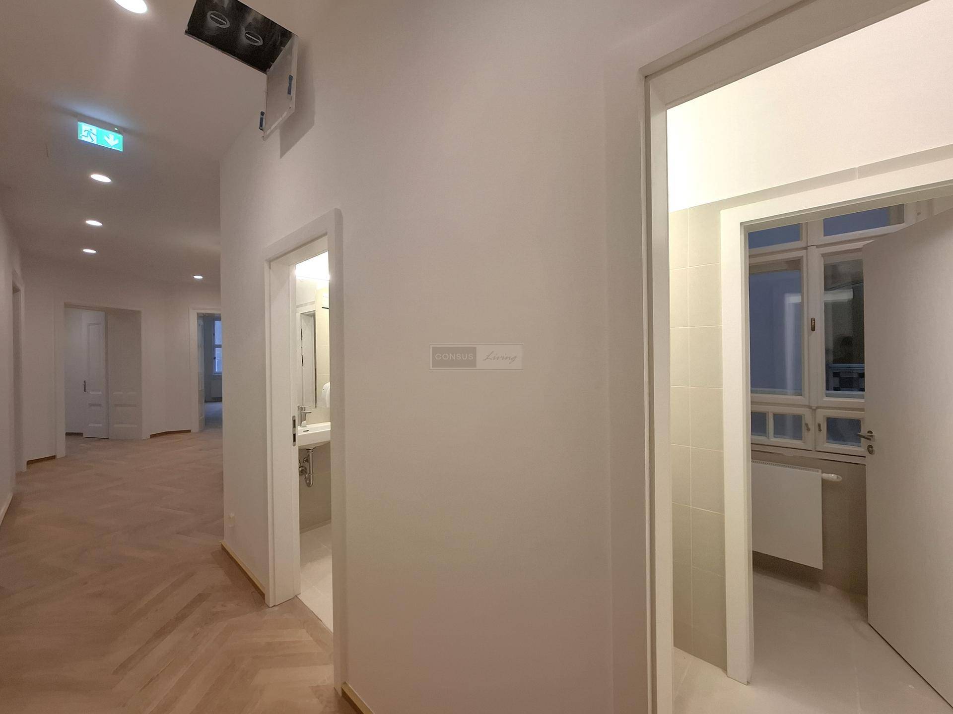 Heller Flur mit Fischgrätparkett, der einen Blick in ein modernes Badezimmer mit Fenster bietet.