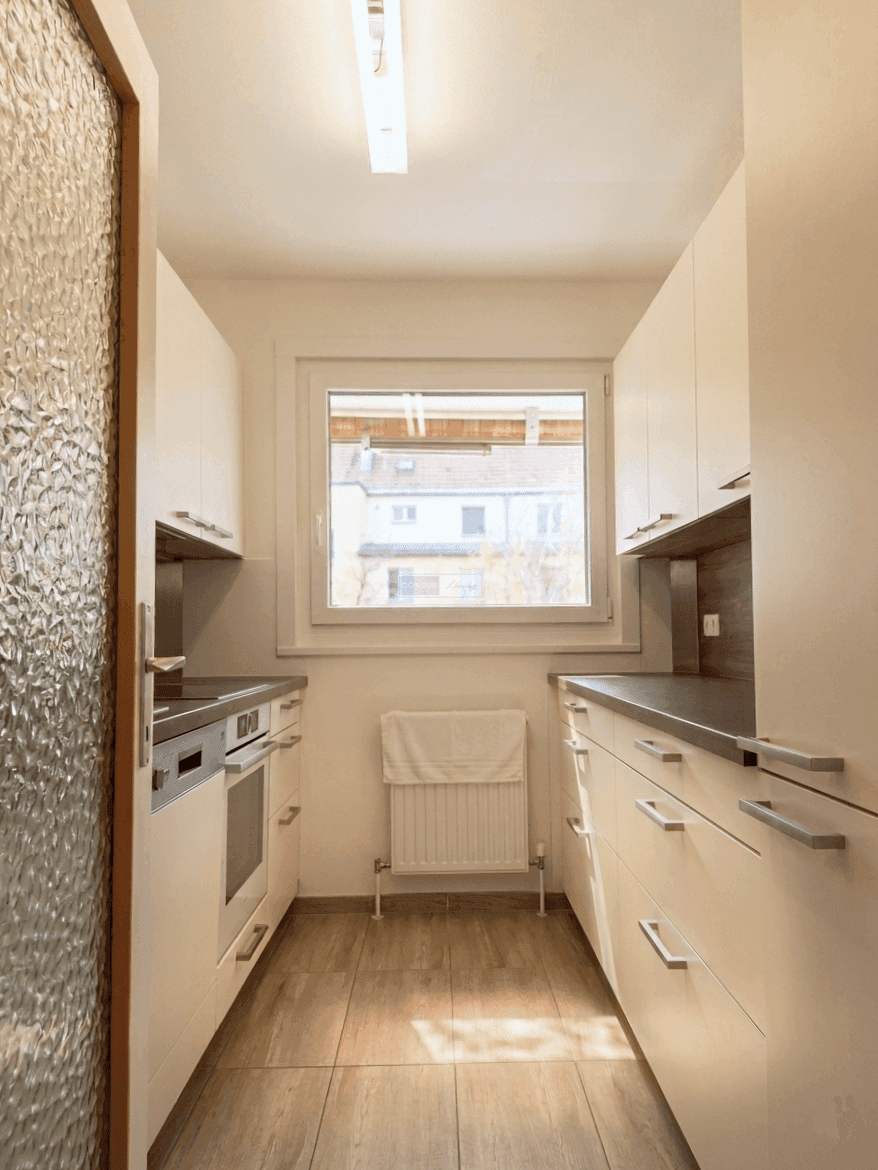 Funktionale Küche mit weißen Schränken, integrierten Geräten und einem Fenster.