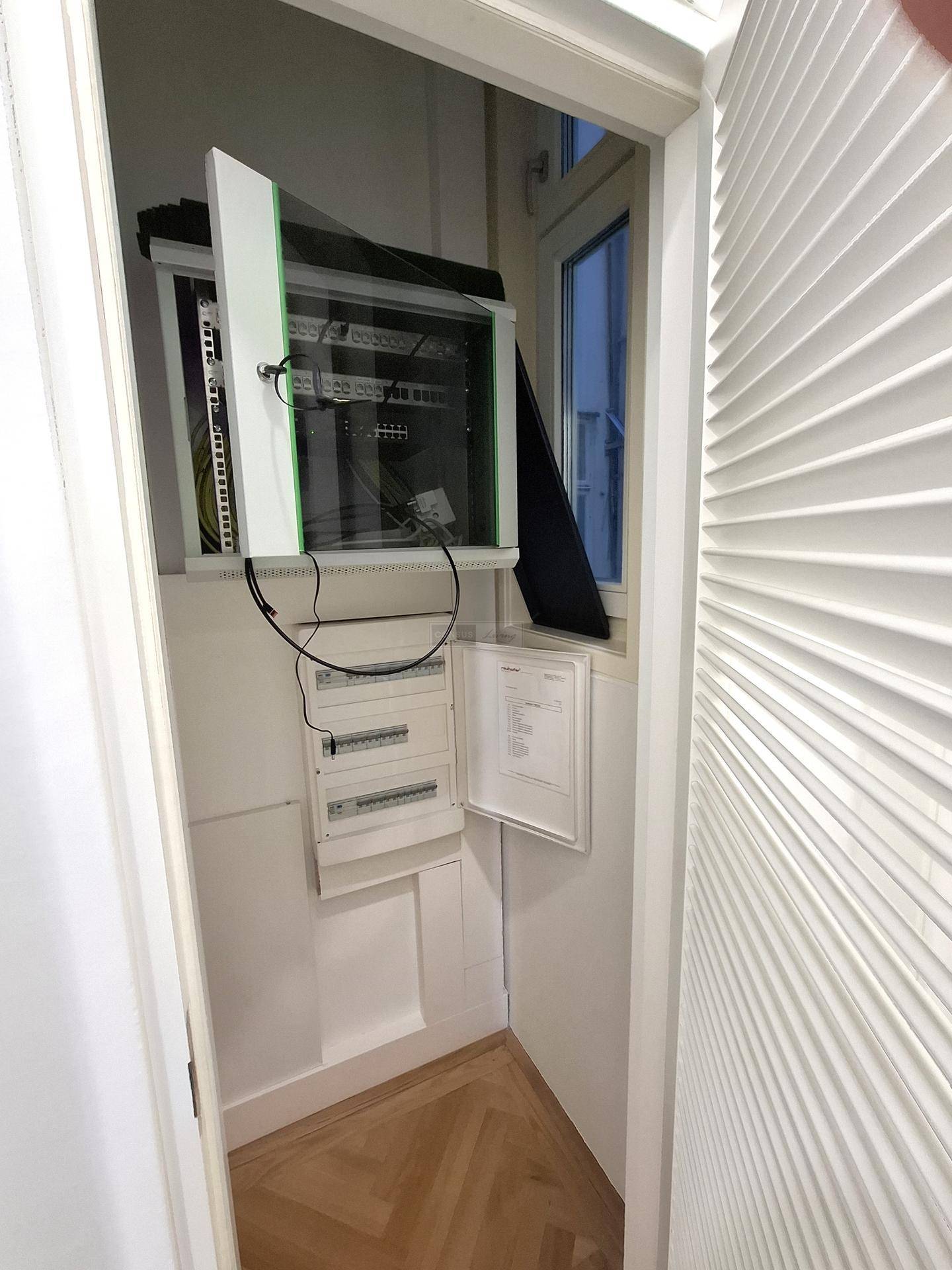Kleiner Abstellraum mit einem Serverschrank und einem Sicherungskasten, neben einem Fenster gelegen.