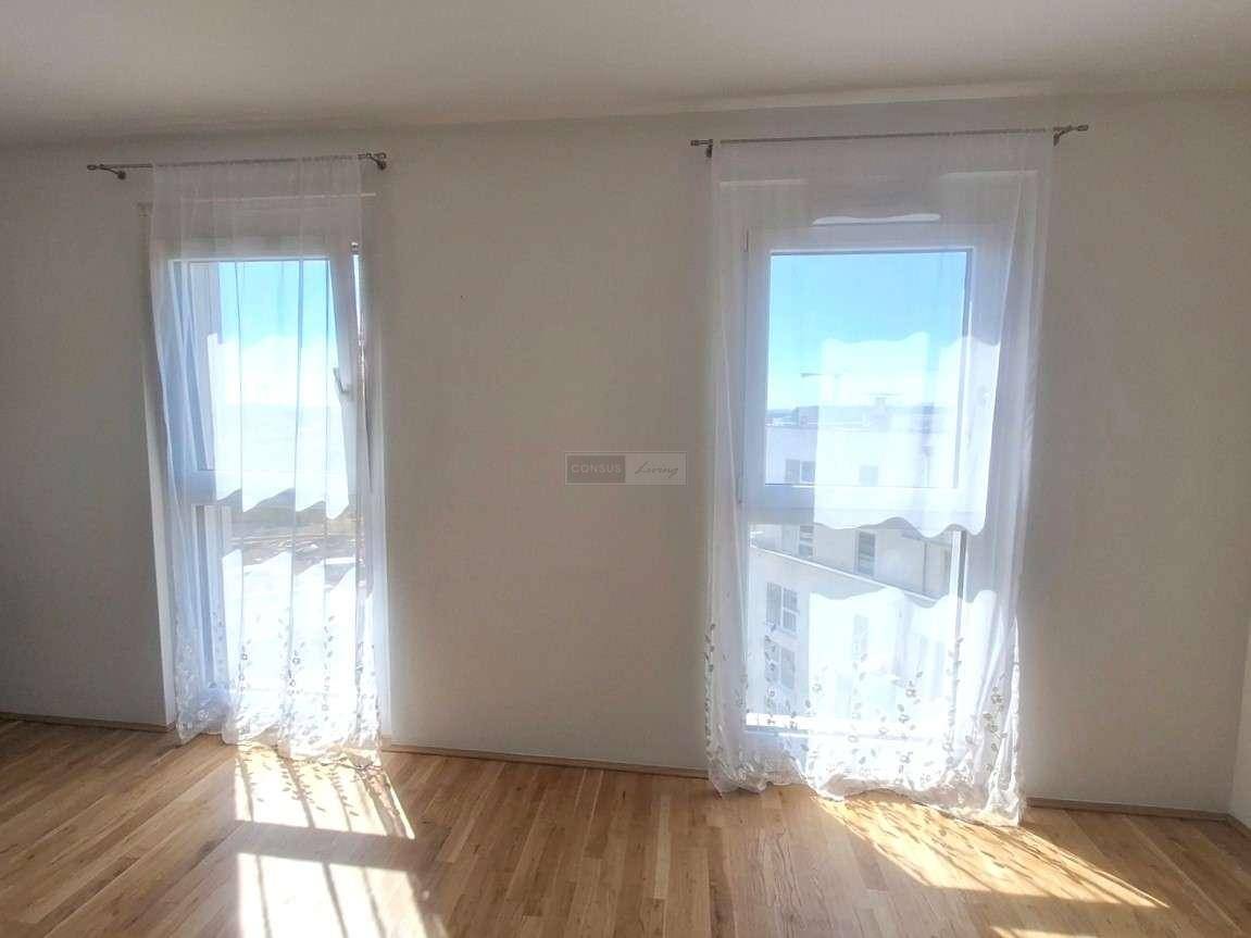 Helles Zimmer mit zwei großen Fenstern, hellem Parkettboden und viel Tageslicht.