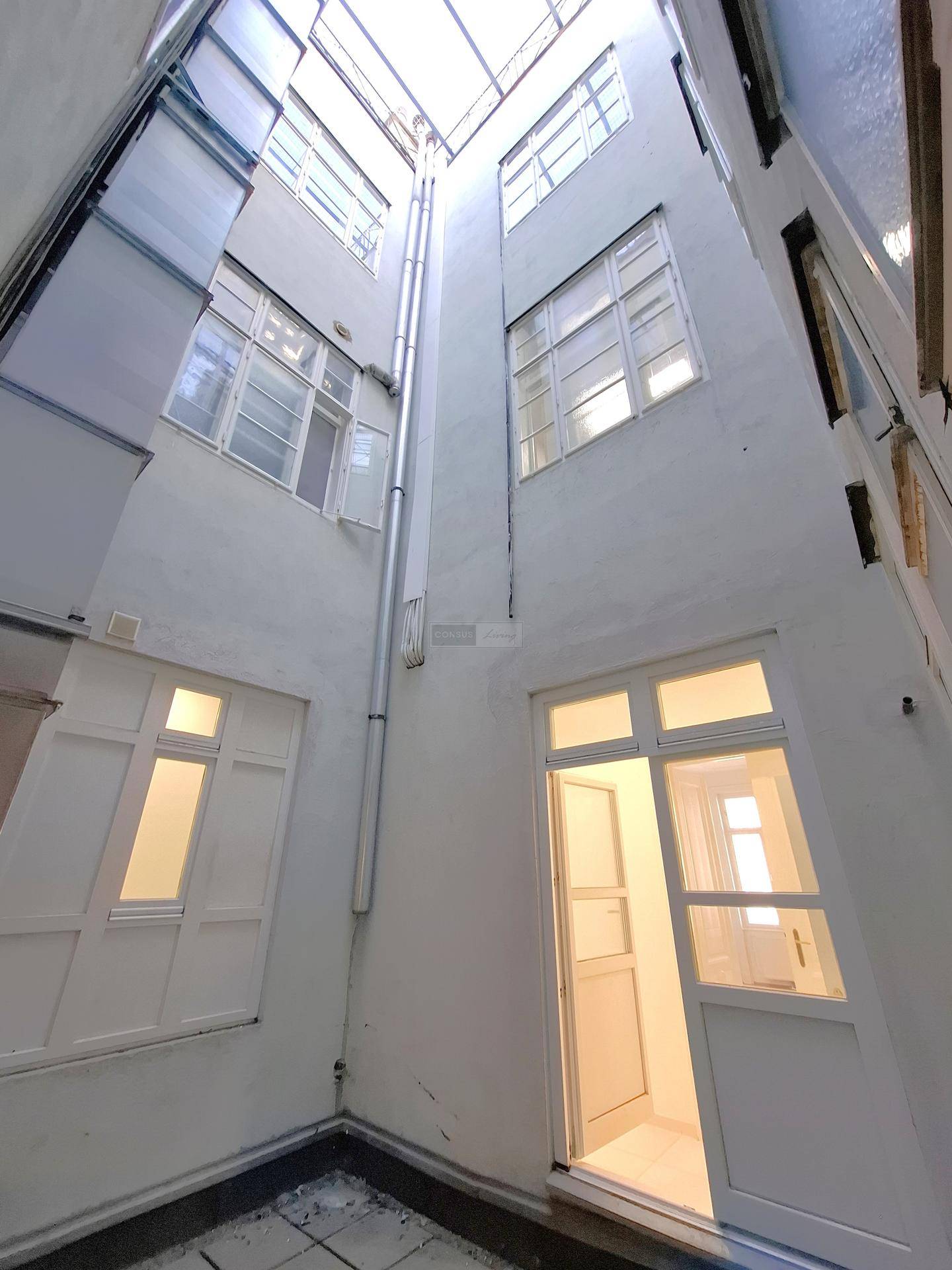 Blick in einen hellen Innenhof mit mehreren Fenstern und Türen, die zu den Wohneinheiten führen.