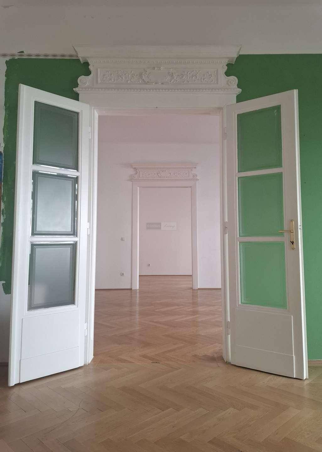 Detailansicht der verzierten Doppeltüren mit Glaseinsätzen, die zwei helle Räume verbinden.