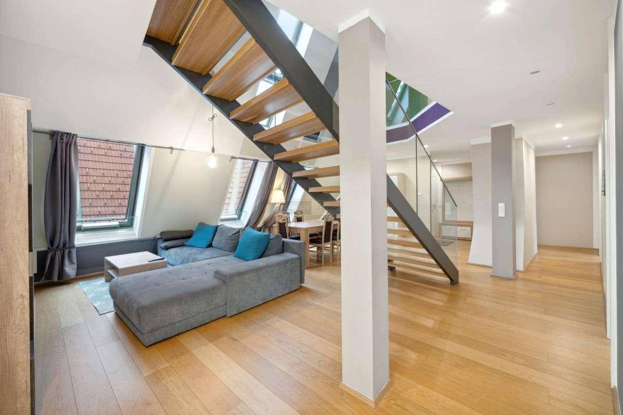 Helles Wohnzimmer mit großem Ecksofa, Holzboden und offener Treppe zum oberen Bereich.