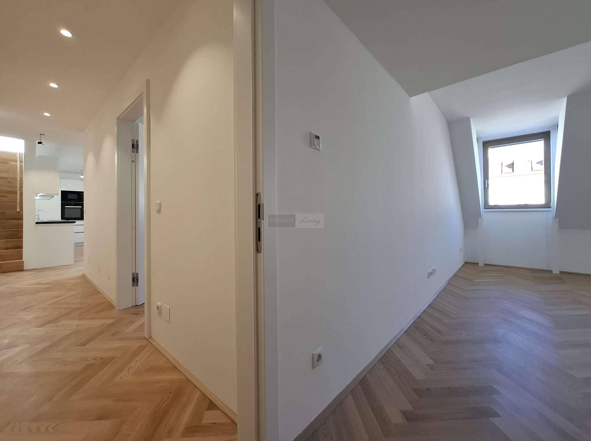Heller Übergangsbereich mit Fischgrätparkett und Fenster, das viel Tageslicht hereinlässt.
