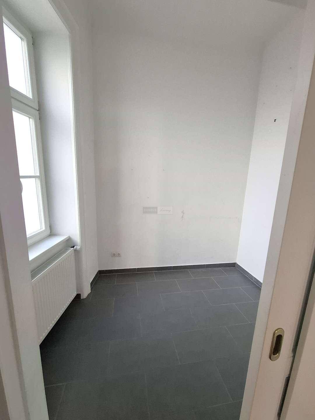 Kleiner, leerer Raum mit dunklem Fliesenboden und Fenster, vielseitig nutzbar.