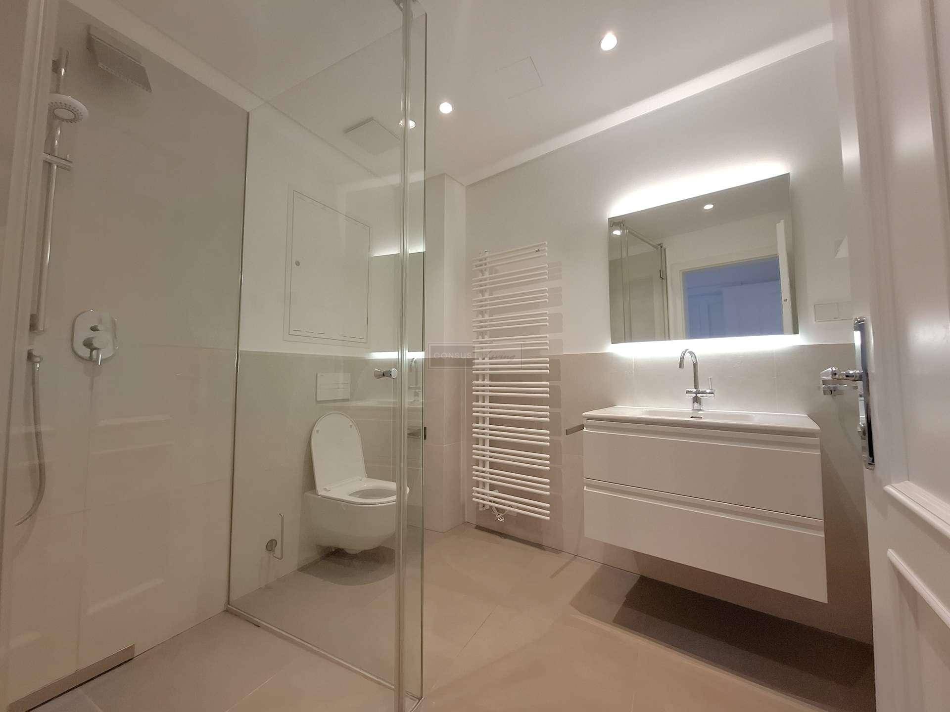 Modernes Badezimmer mit begehbarer Dusche, wandhängendem WC und beleuchtetem Spiegelschrank.