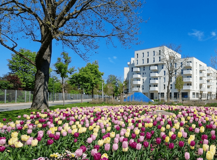 Modernes Wohngebäude umgeben von einer farbenfrohen Tulpenwiese und grünen Bäumen unter blauem Himmel.