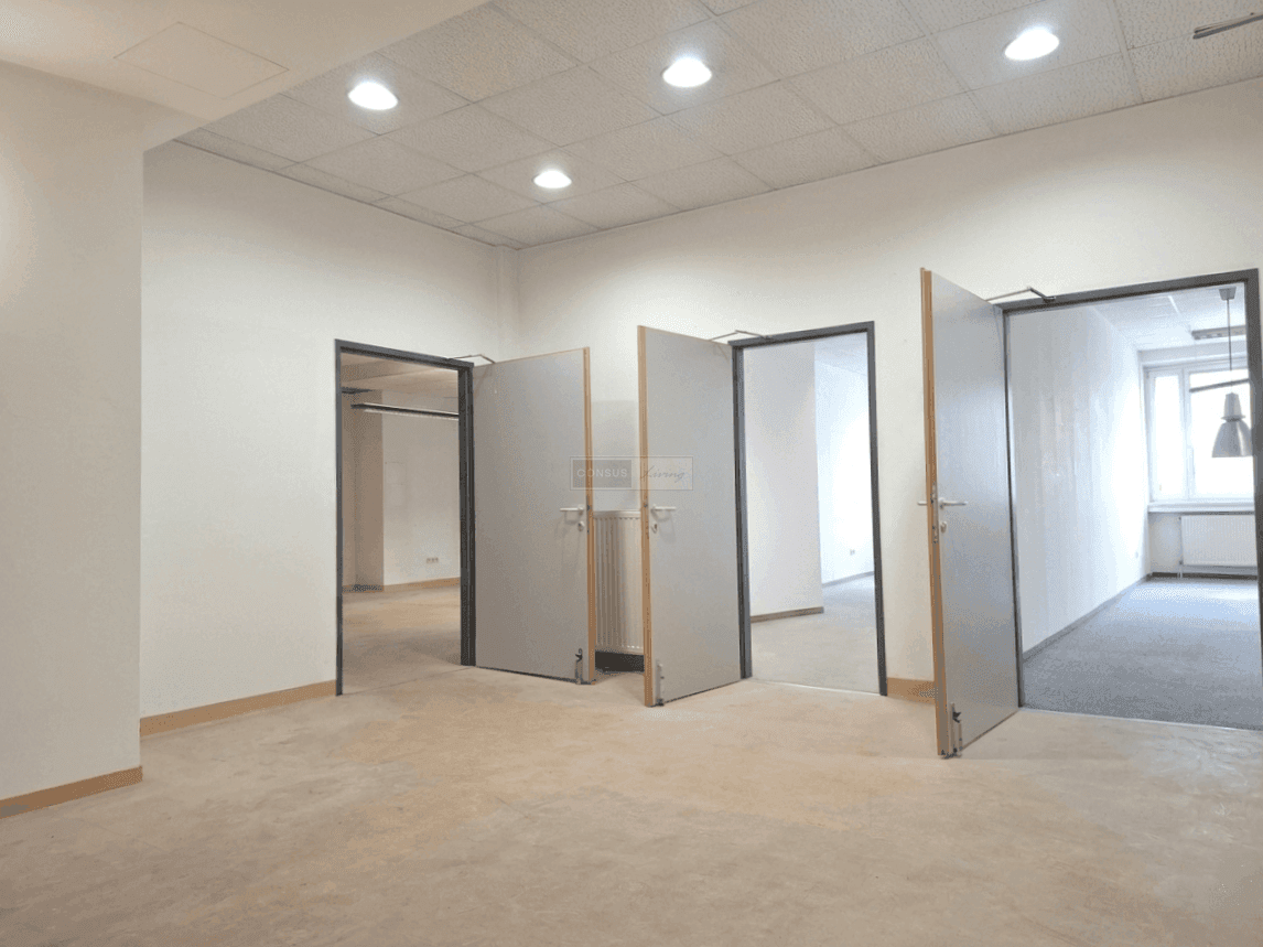 Heller Bürobereich mit mehreren Türen, die zu weiteren Räumen führen, und einer abgehängten Decke.