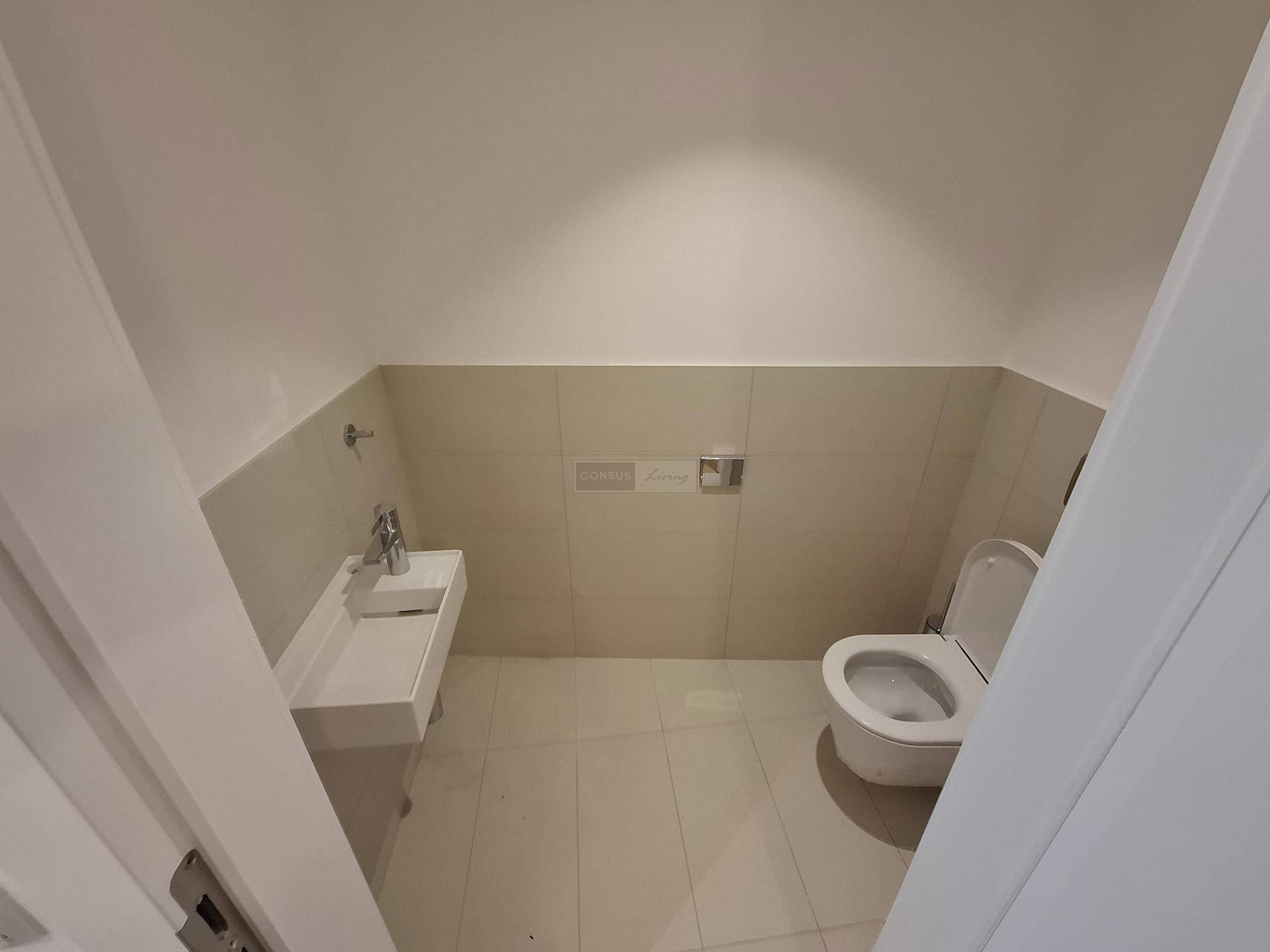Funktionales Gäste-WC mit hellen Fliesen, wandhängender Toilette und kleinem Waschbecken.
