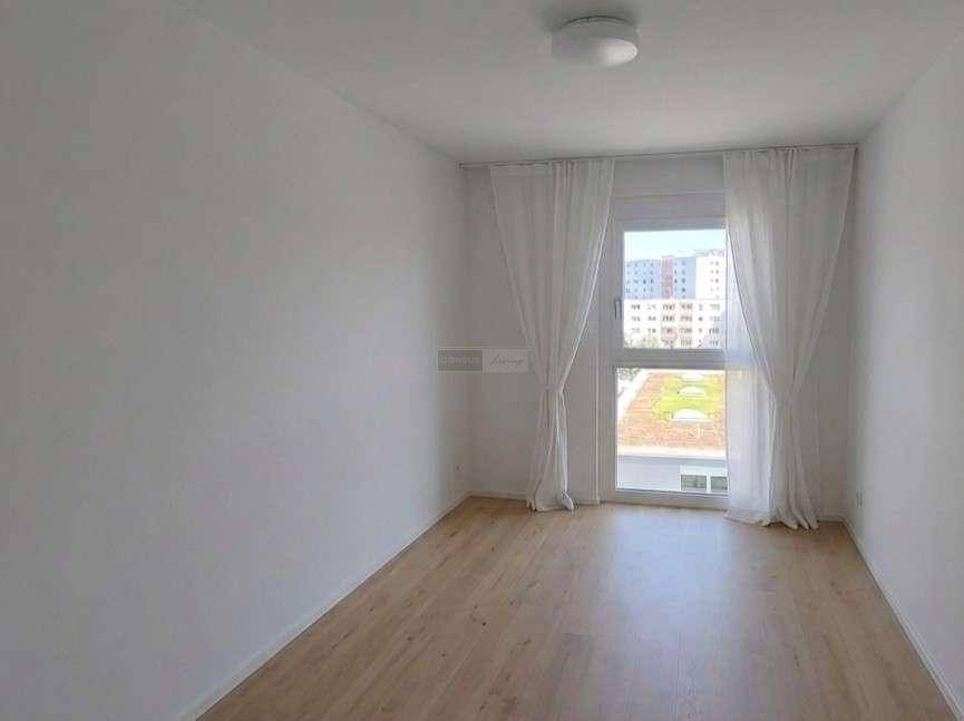 Freundliches Zimmer mit hellem Parkettboden und großem Fenster mit Blick auf eine begrünte Dachfläche.