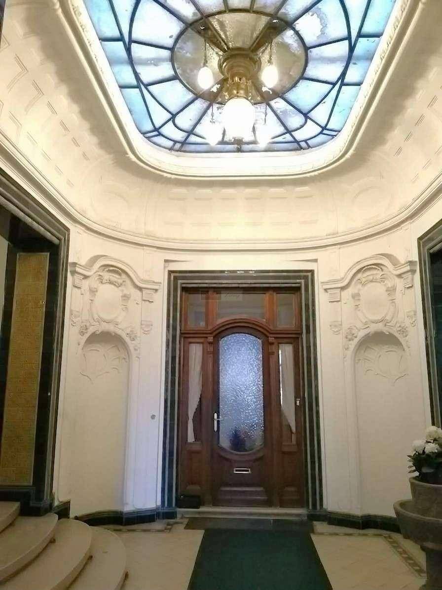 Elegante Eingangshalle mit kunstvoller Holztür, Stuckverzierungen und einem farbigen Glasdachfenster, sehr hell.