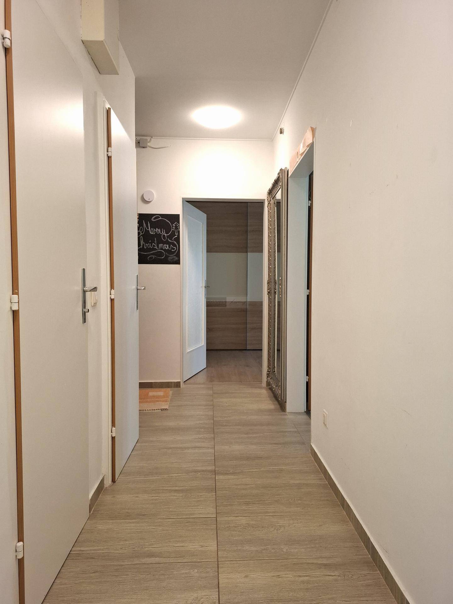 Langer Flur mit hellem Boden, mehreren Türen und einem großen Wandspiegel.