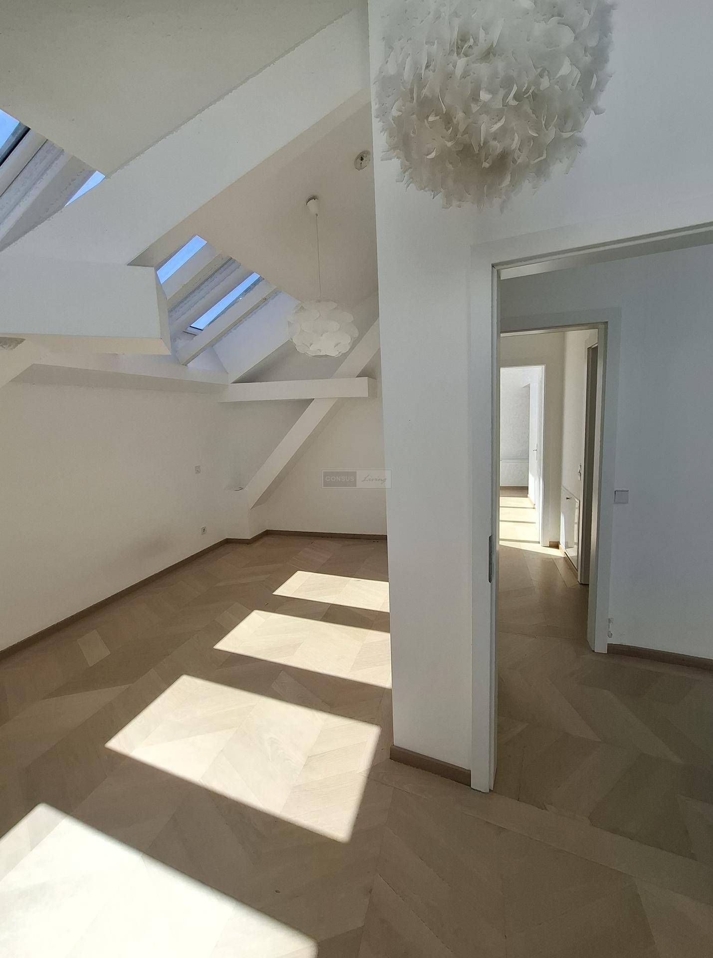 Heller Raum mit Dachschrägen, Parkettboden und großen Dachfenstern, die viel Licht hereinlassen.