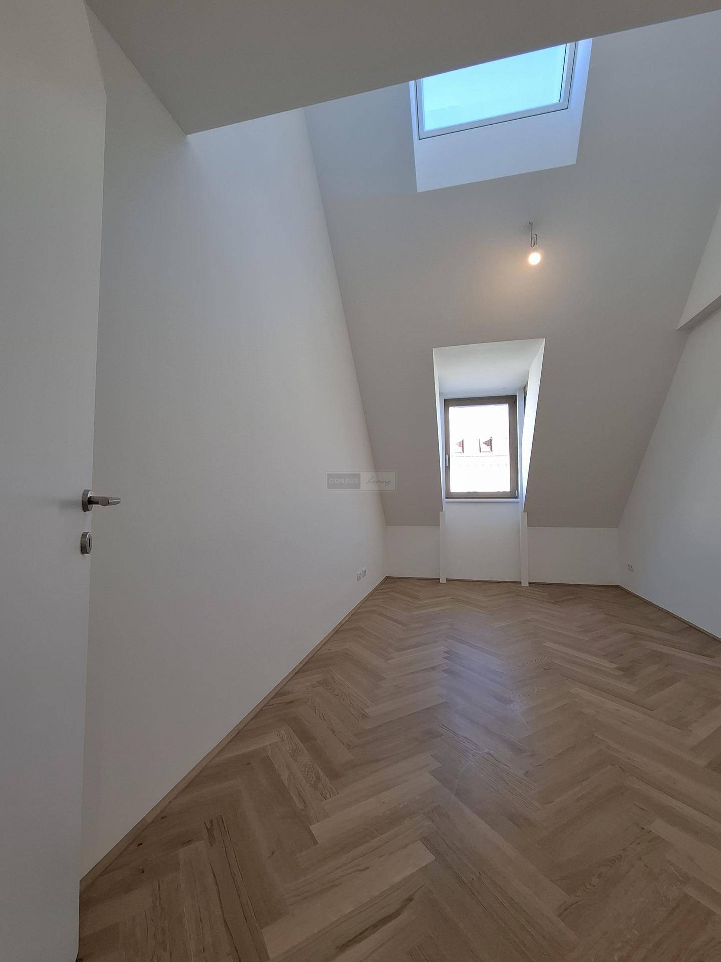 Helles Zimmer mit Fischgrätparkett, Dachschräge und Dachfenster für viel Tageslicht.