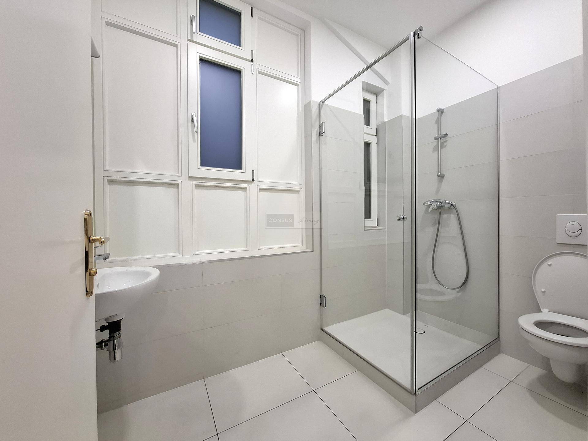 Modernes Badezimmer mit großer Glasdusche, wandhängendem WC und Fenster für natürliche Belüftung.