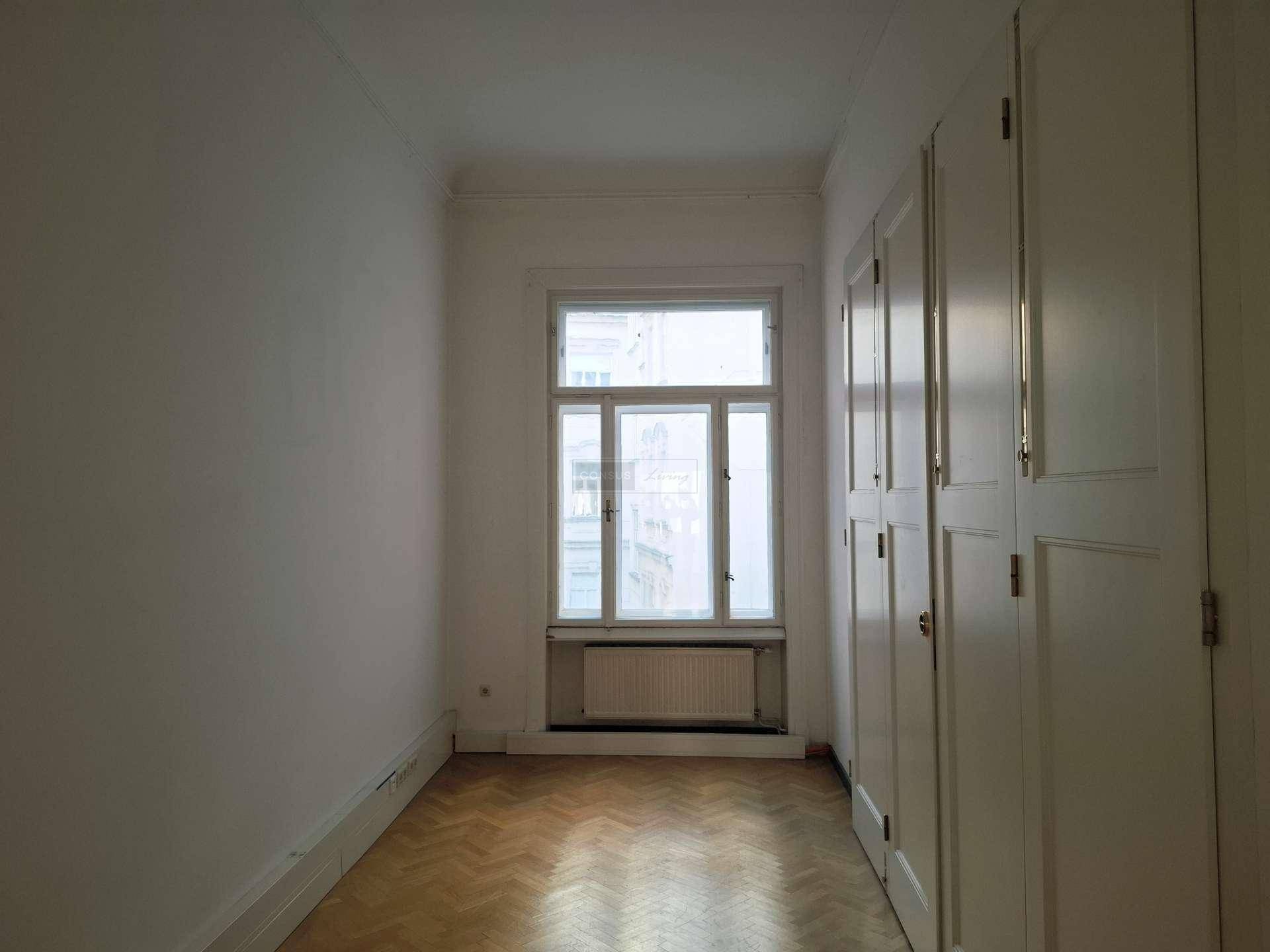 Schmaler, leerer Raum mit Fischgrätparkett, einem Fenster und praktischen Einbauschränken entlang der Wand.