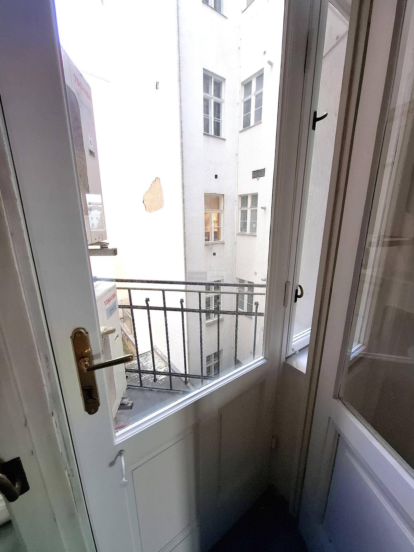 Kleiner Balkon mit Blick in einen ruhigen Innenhof, umgeben von weißen Gebäudefassaden.