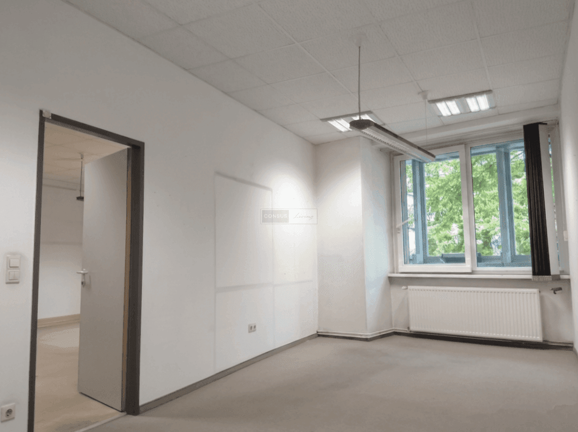 Kleinerer Büroraum mit großen Fenstern, die viel Tageslicht hereinlassen, und einem Heizkörper unter dem Fenster.