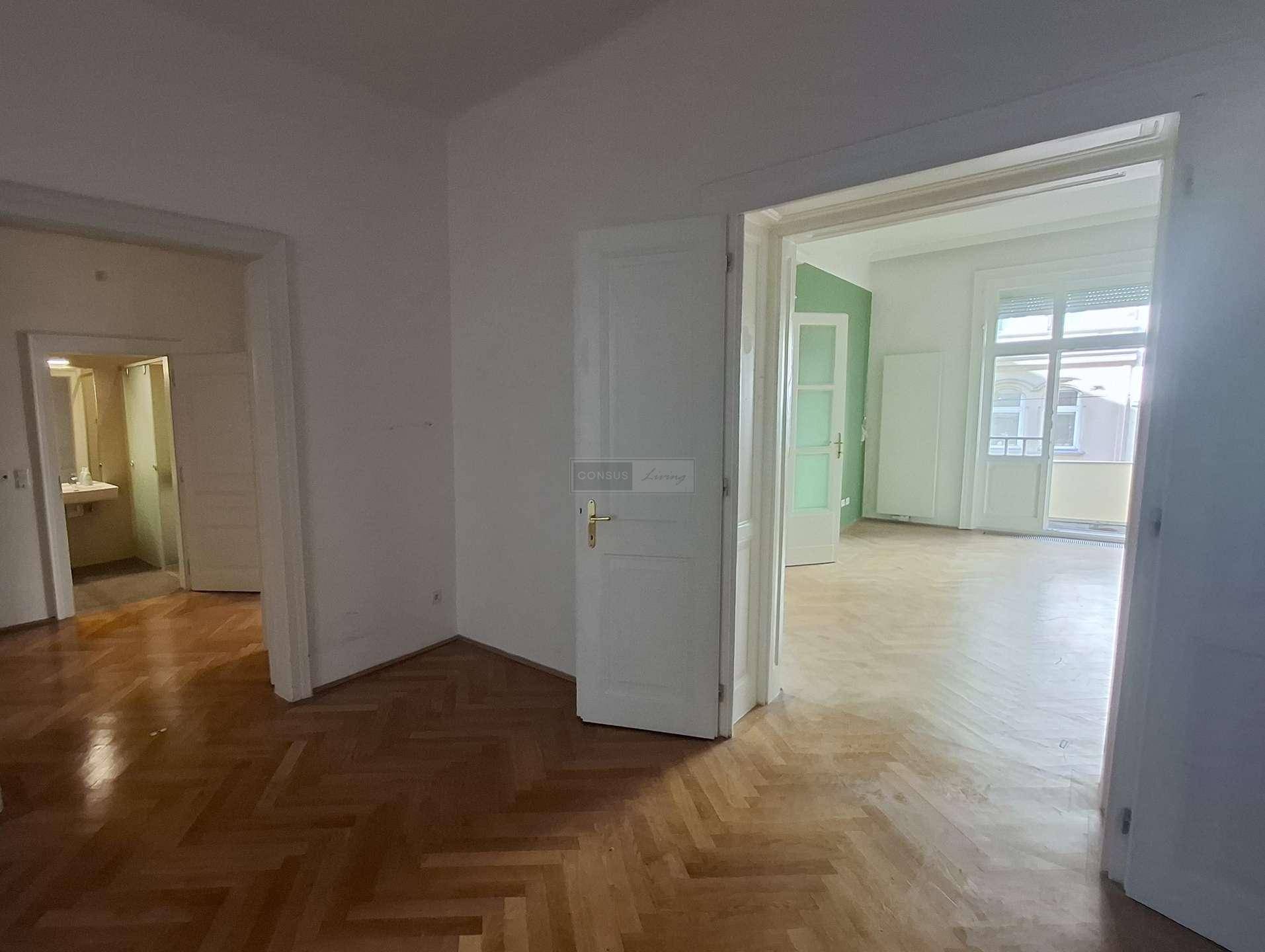 Blick durch einen leeren Raum mit Parkettboden, der zu einem Badezimmer und einem weiteren Zimmer führt.