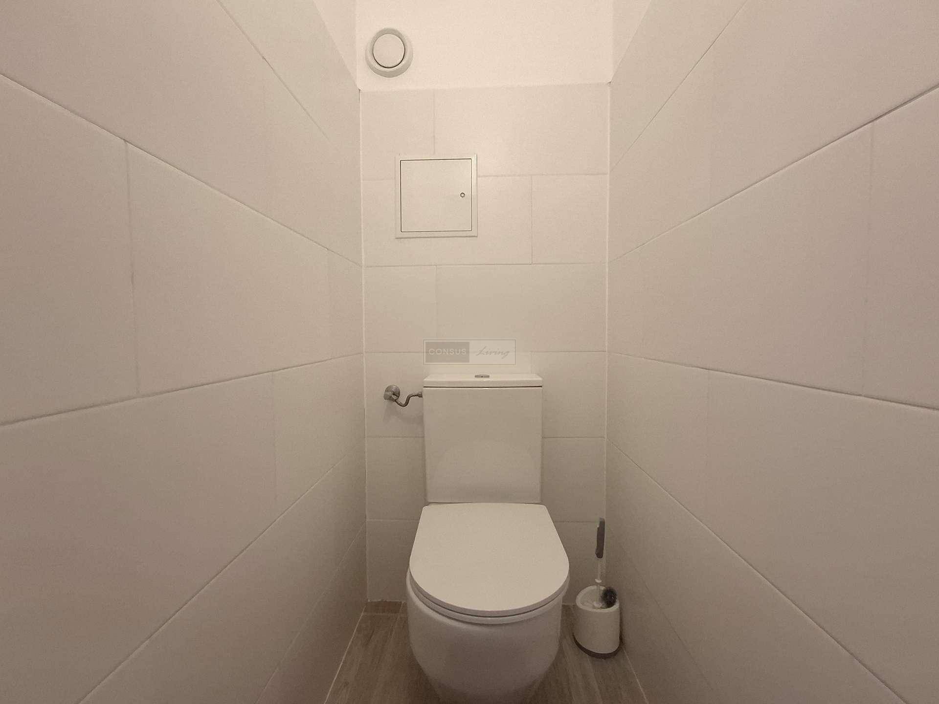 Separates WC mit wandhängender Toilette und hellen Fliesen an den Wänden.