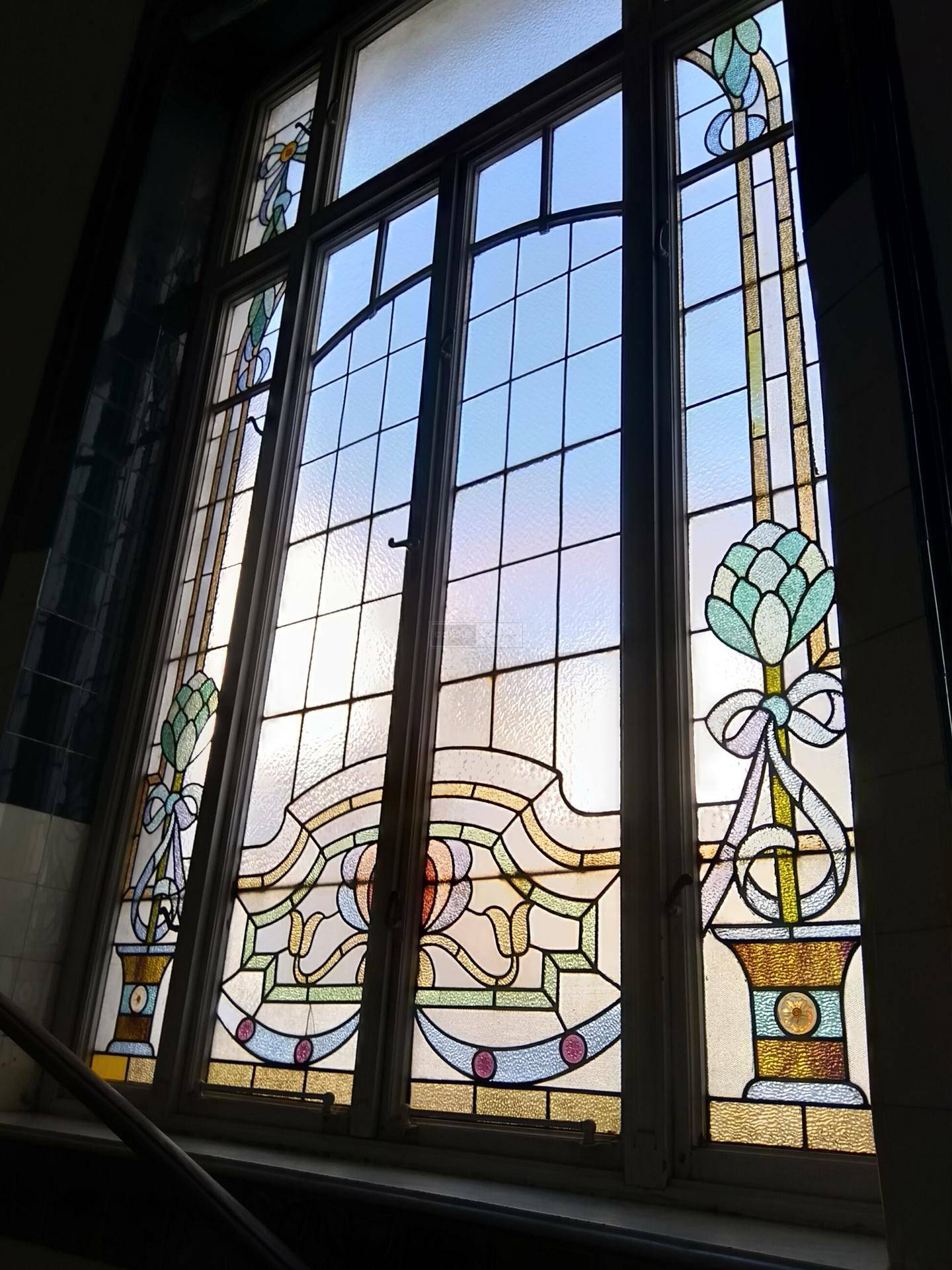 Farbenfrohes Buntglasfenster mit kunstvollen Mustern, das viel Licht in den Treppenbereich des Altbaus bringt.