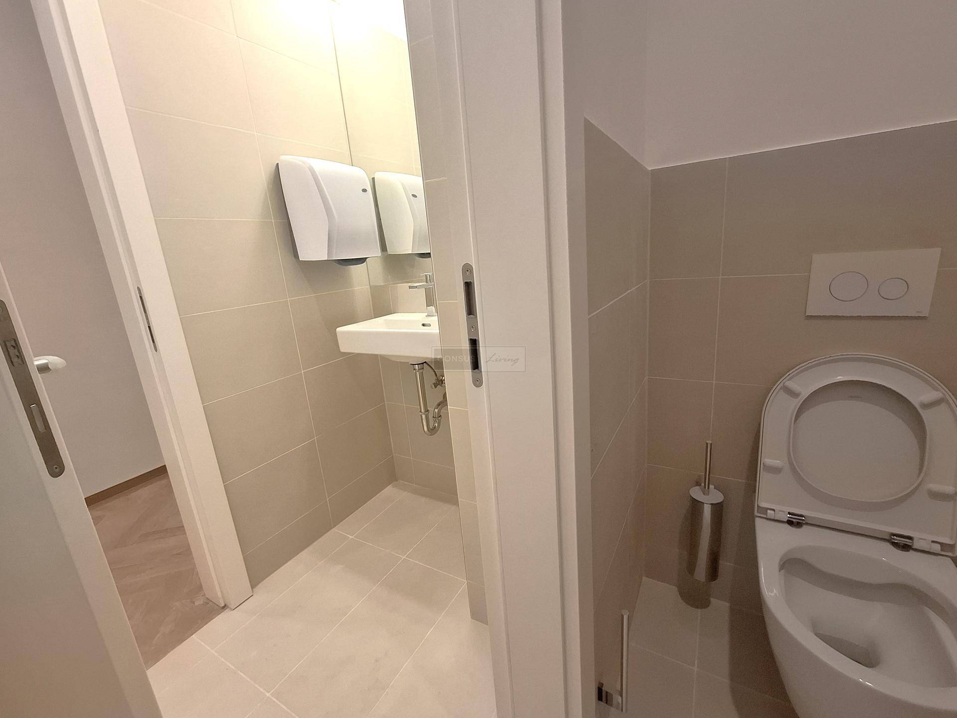 Modernes Gäste-WC mit Wand-WC, kleinem Waschbecken und hellen Fliesen.
