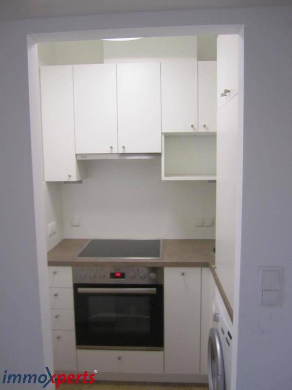 Kleine Einbauküche mit Backofen, Induktionskochfeld, Spüle und weißen Schränken.
