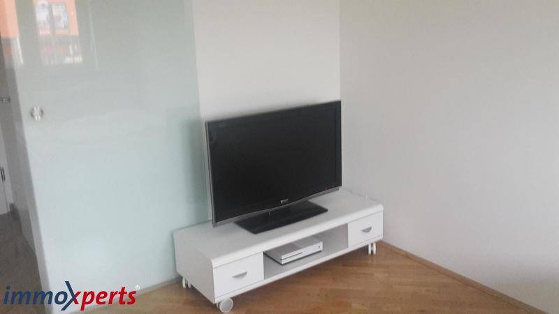 Wohnbereich mit Fernseher auf einem weißen TV-Möbel und hellem Holzboden.