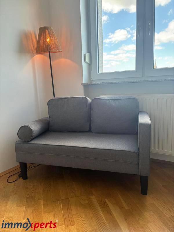 Gemütliches Wohnzimmer mit kleinem Sofa, Stehlampe und Fenster für natürliche Beleuchtung.