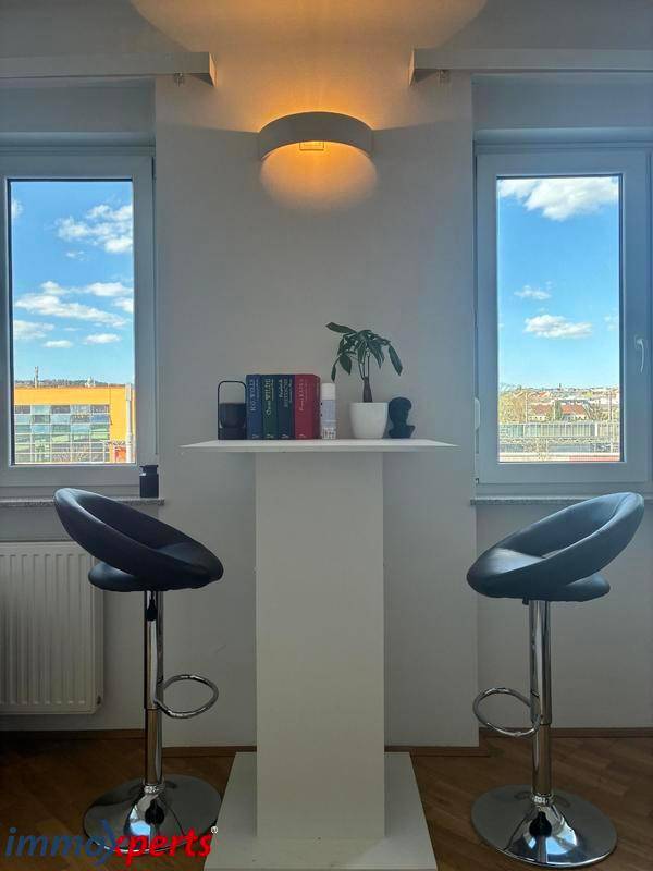 Heller Bereich mit Bartisch und zwei Barhockern, umgeben von Fenstern mit weitem Ausblick.