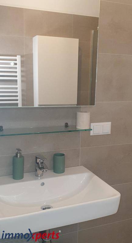 Modernes Badezimmer mit Waschbecken, Spiegel und Spiegelschrank, hell gefliest.