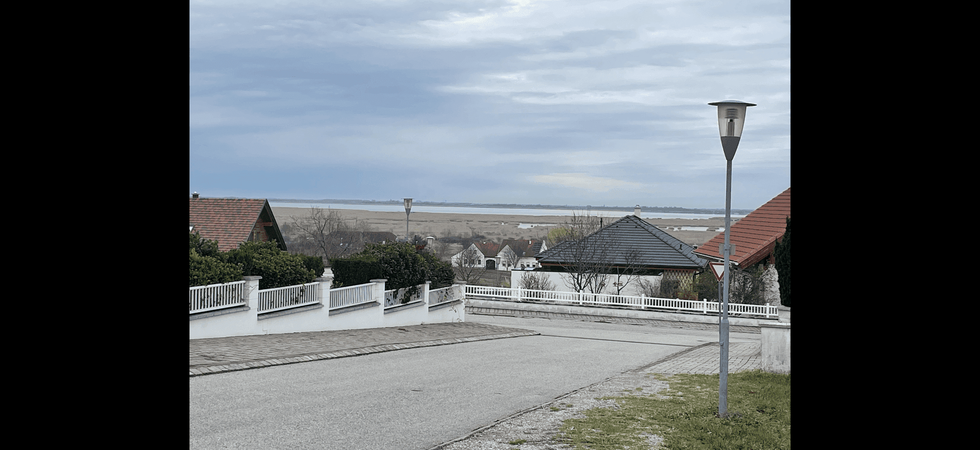 Straße mit Wohnhäusern und weitem Blick auf eine Wasserfläche und die umliegende Landschaft.