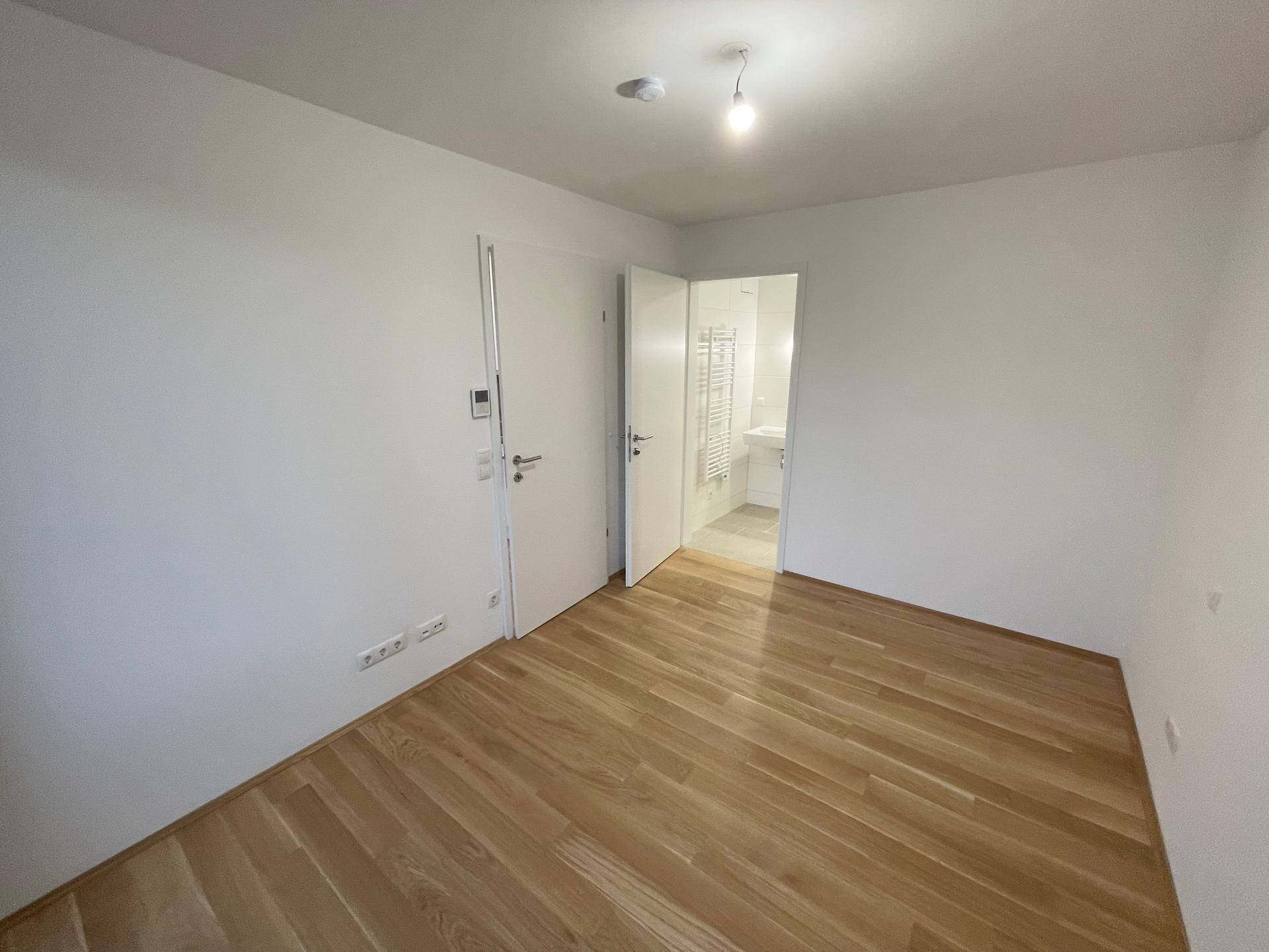 Helles Schlafzimmer mit Eichenparkettboden und Zugang zu einem angrenzenden Badezimmer.