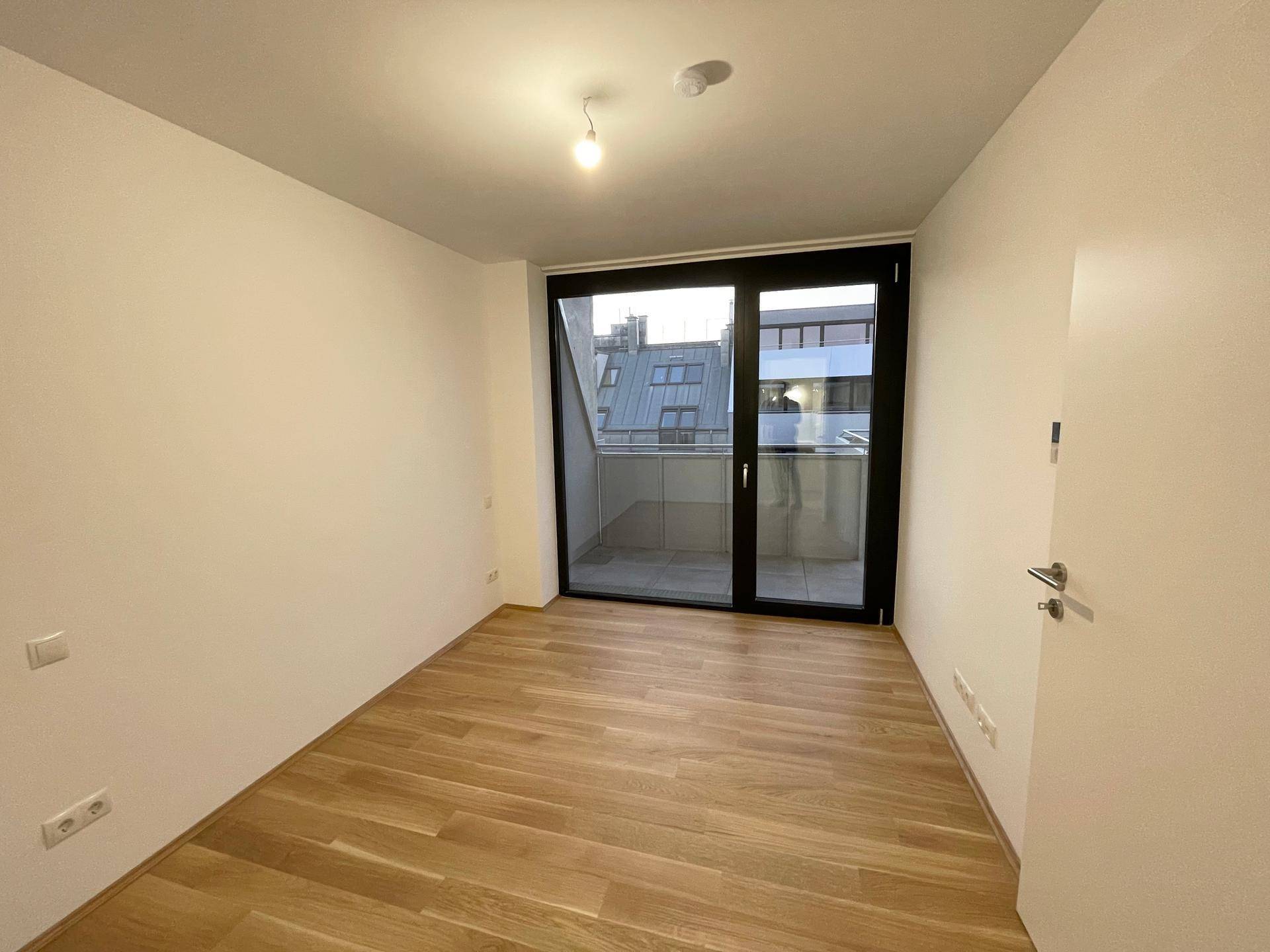 Helles Schlafzimmer mit Holzboden und großen Schiebetüren, die auf einen Balkon führen.