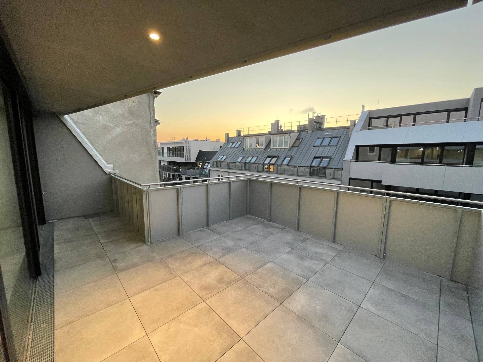 Heller Balkon mit Fliesenboden und Blick auf die umliegende Stadtlandschaft bei Sonnenuntergang.