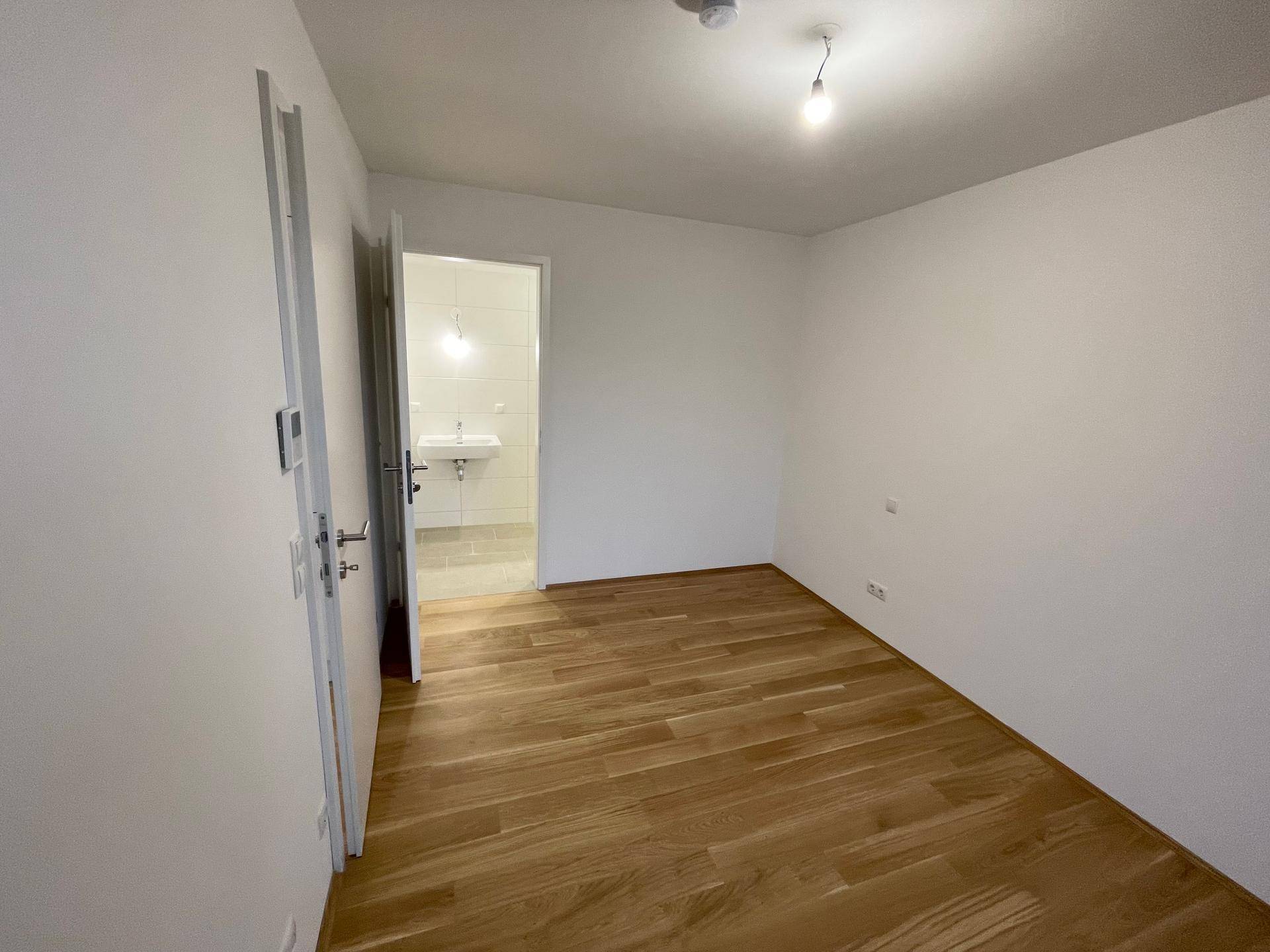 Leeres Schlafzimmer mit hellem Holzboden und direktem Zugang zu einem modernen Badezimmer.