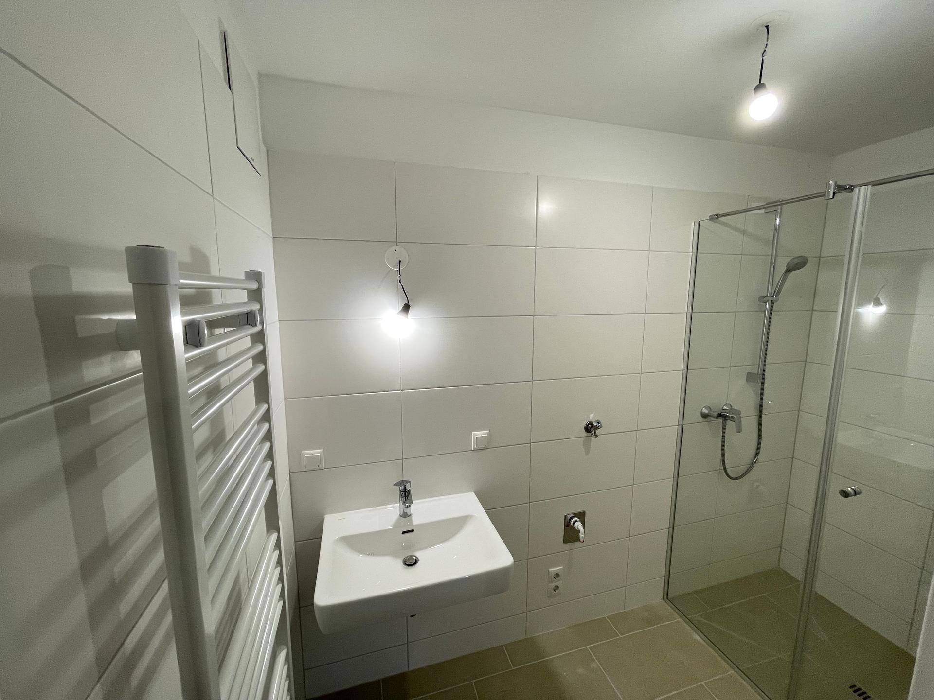 Modernes Badezimmer mit Duschkabine, wandmontiertem Waschbecken und beheiztem Handtuchhalter.