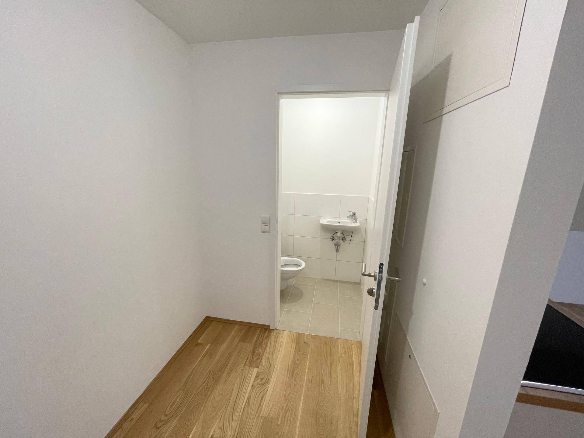 Kleines Gäste-WC mit hellen Fliesen, wandmontierter Toilette und Handwaschbecken.