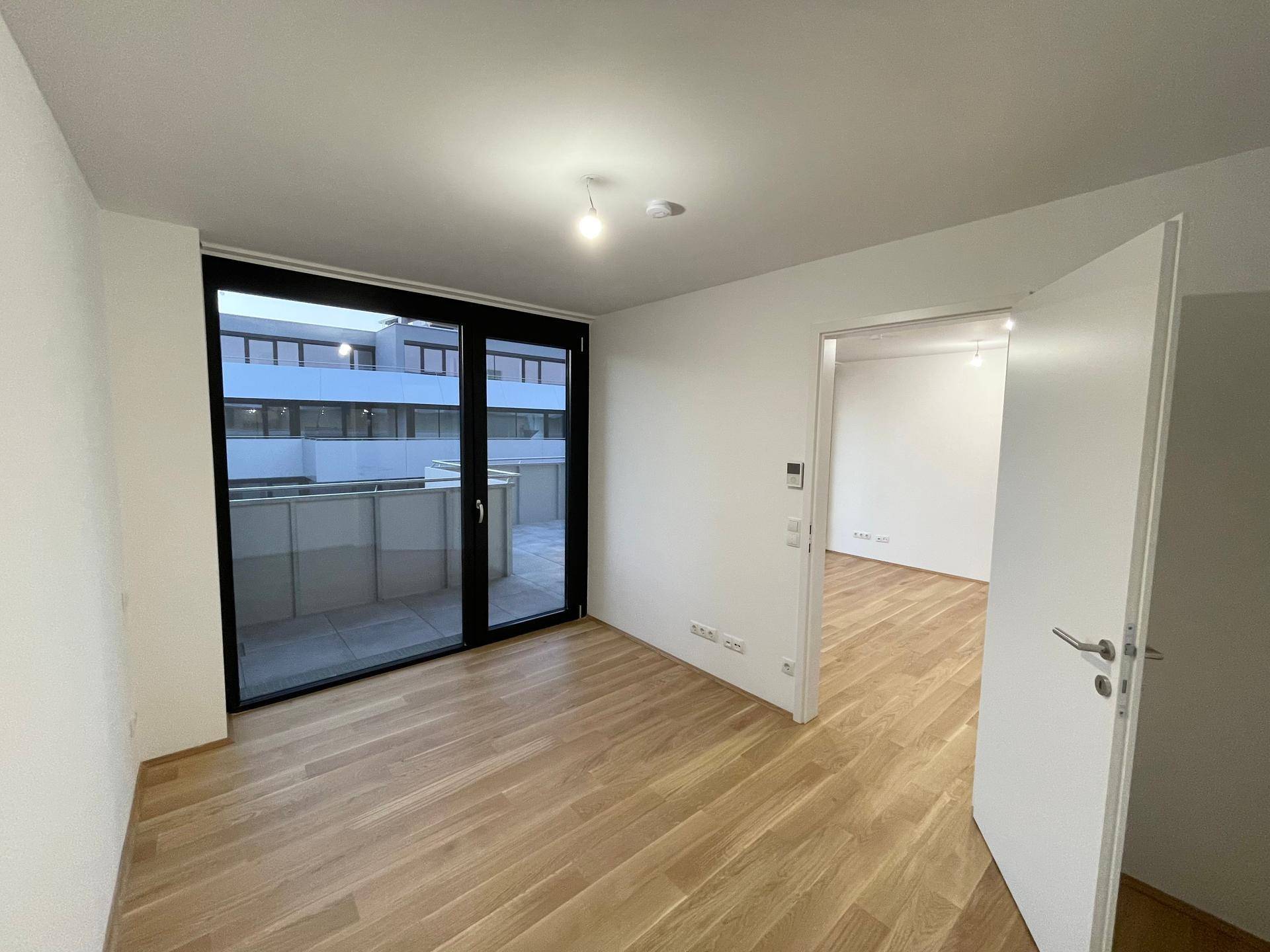 Geräumiges Schlafzimmer mit Parkettboden und Zugang zu einem Außenbereich durch große Fenster.