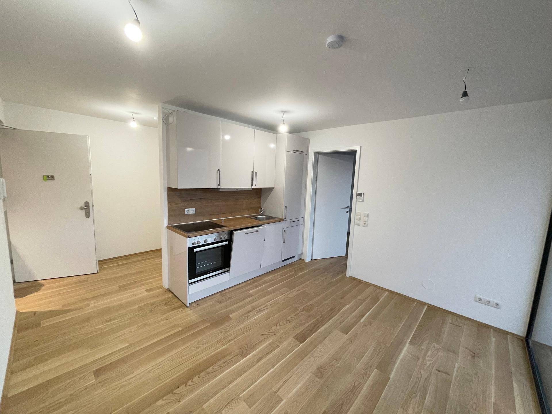 Offener Wohnbereich mit moderner weißer Küchenzeile, Holzboden und viel Tageslicht.
