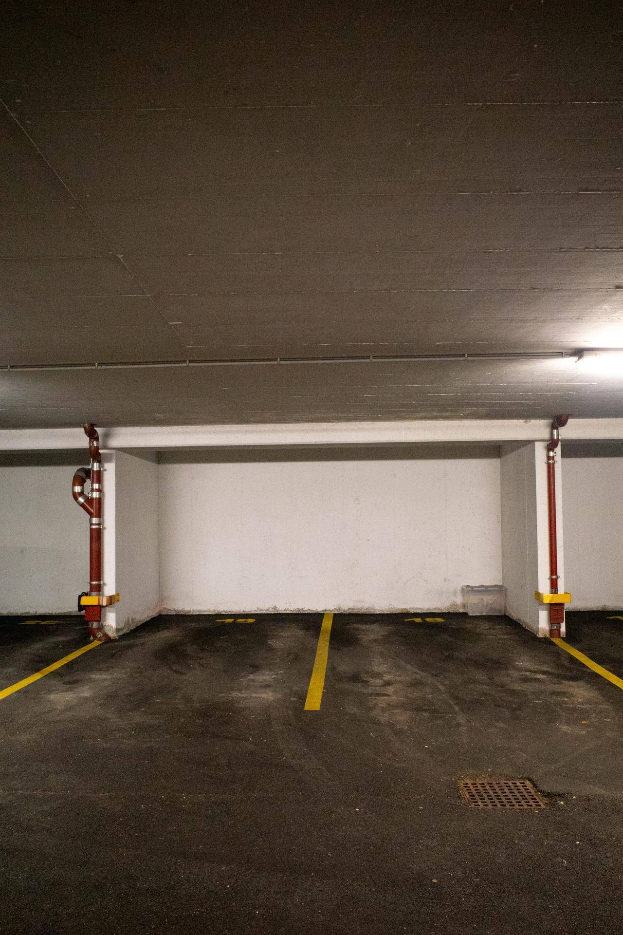Leerer Tiefgaragenstellplatz mit gelben Bodenmarkierungen und sichtbaren Rohren.