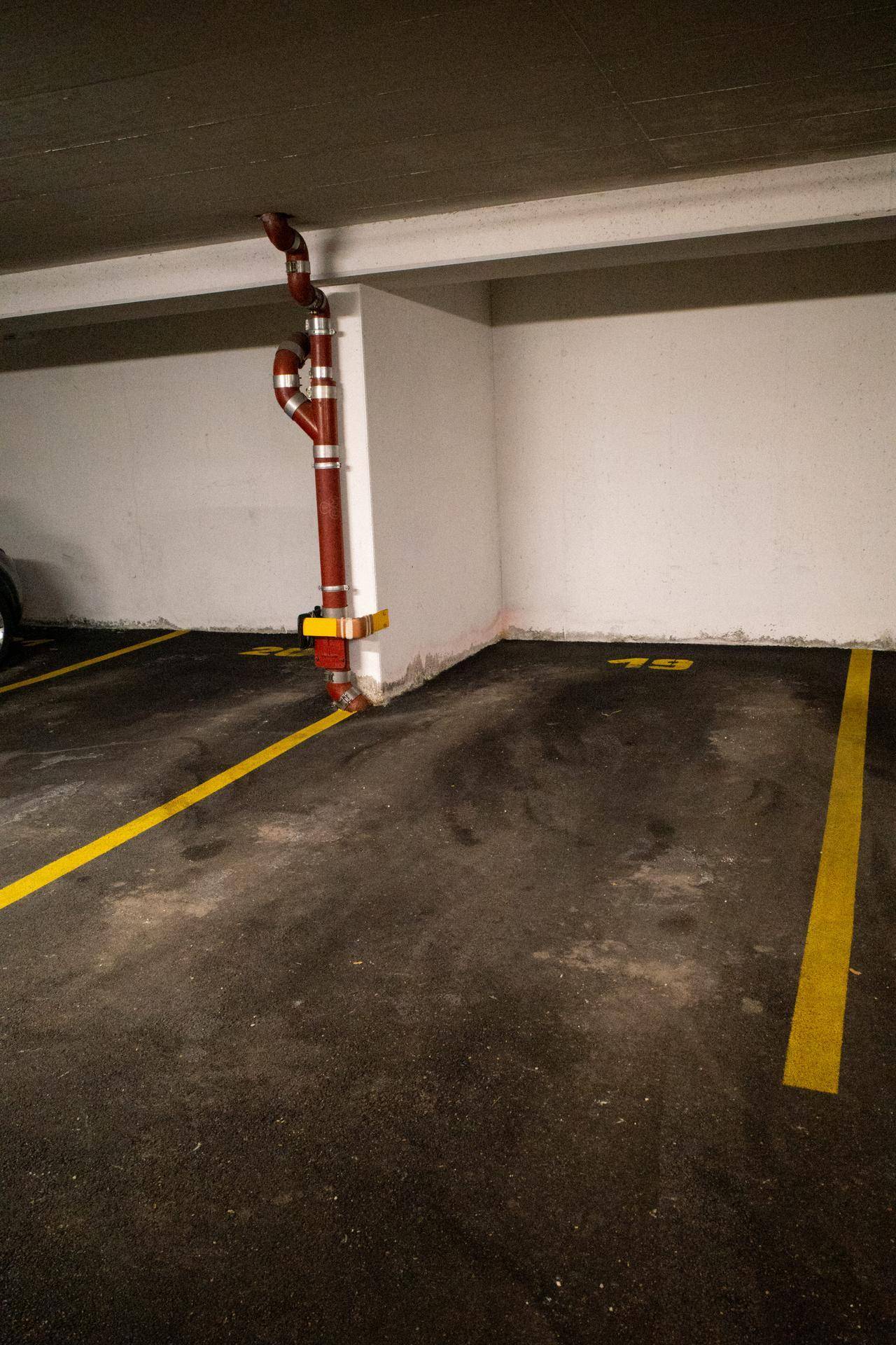 Detailansicht eines leeren Tiefgaragenstellplatzes mit gelben Linien und Rohren.