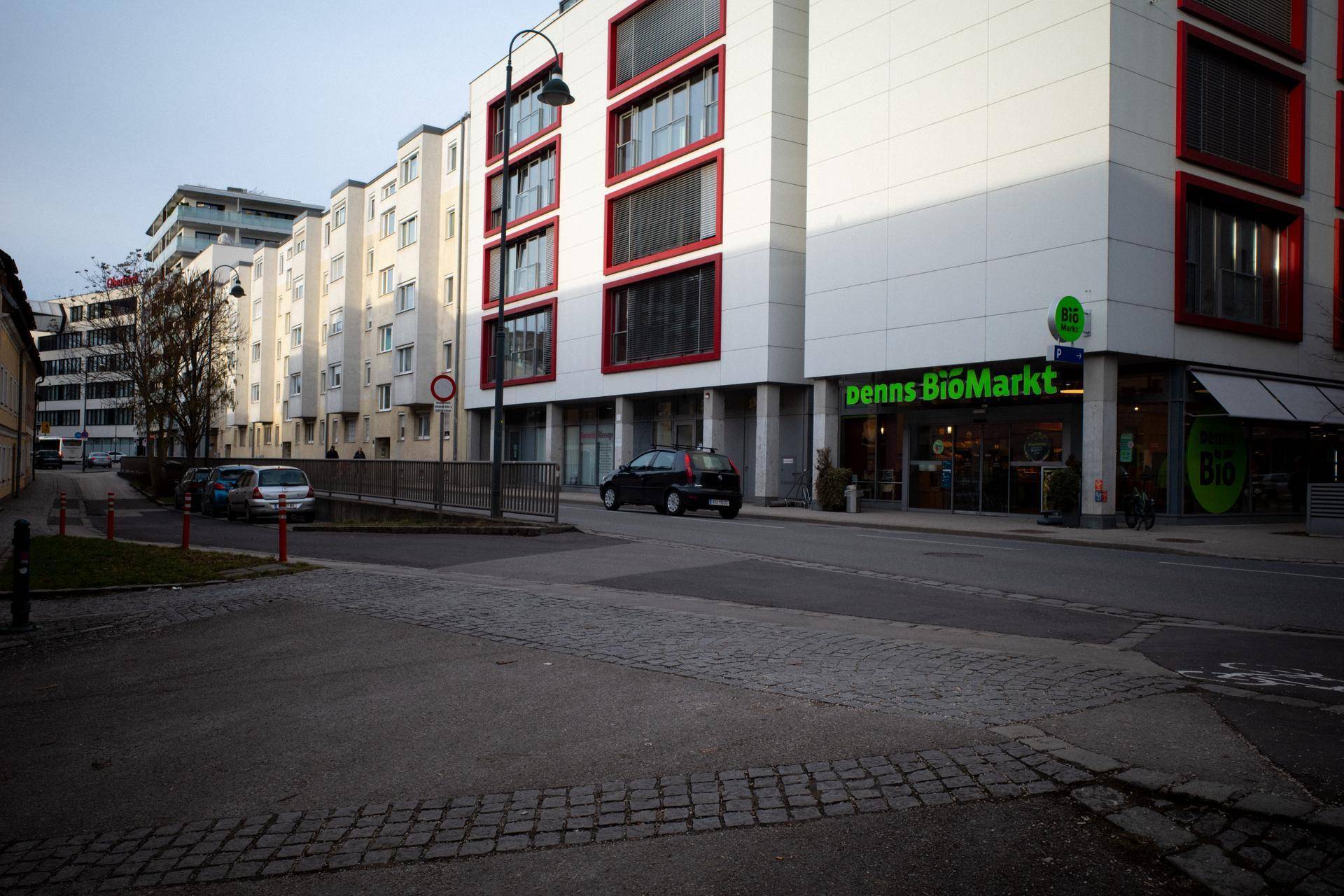 Straßenansicht mit modernen Gebäuden, Geschäften und geparkten Autos in urbaner Umgebung.