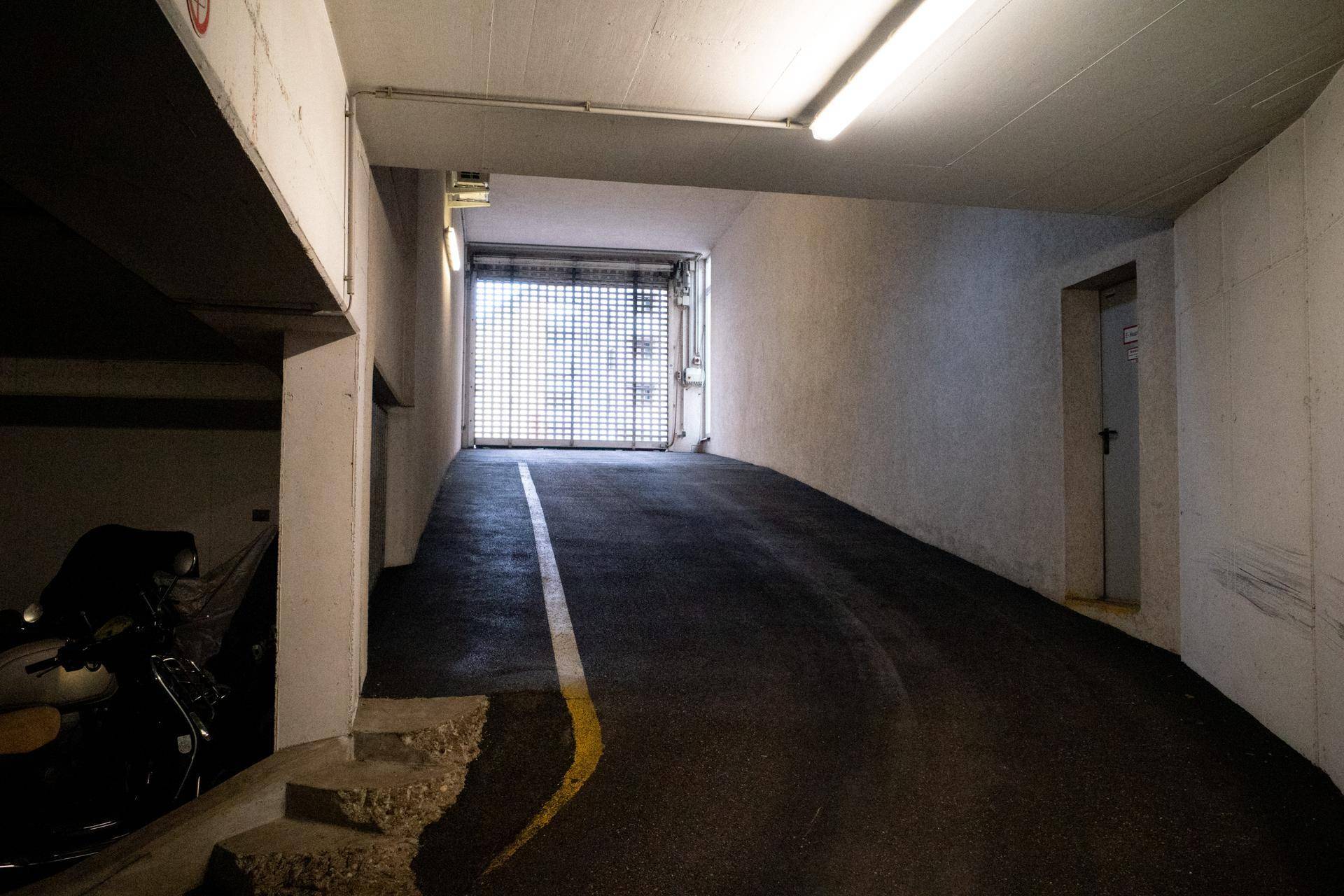 Zufahrtsrampe zur Tiefgarage mit Rolltor am Ende und hellen Wänden.