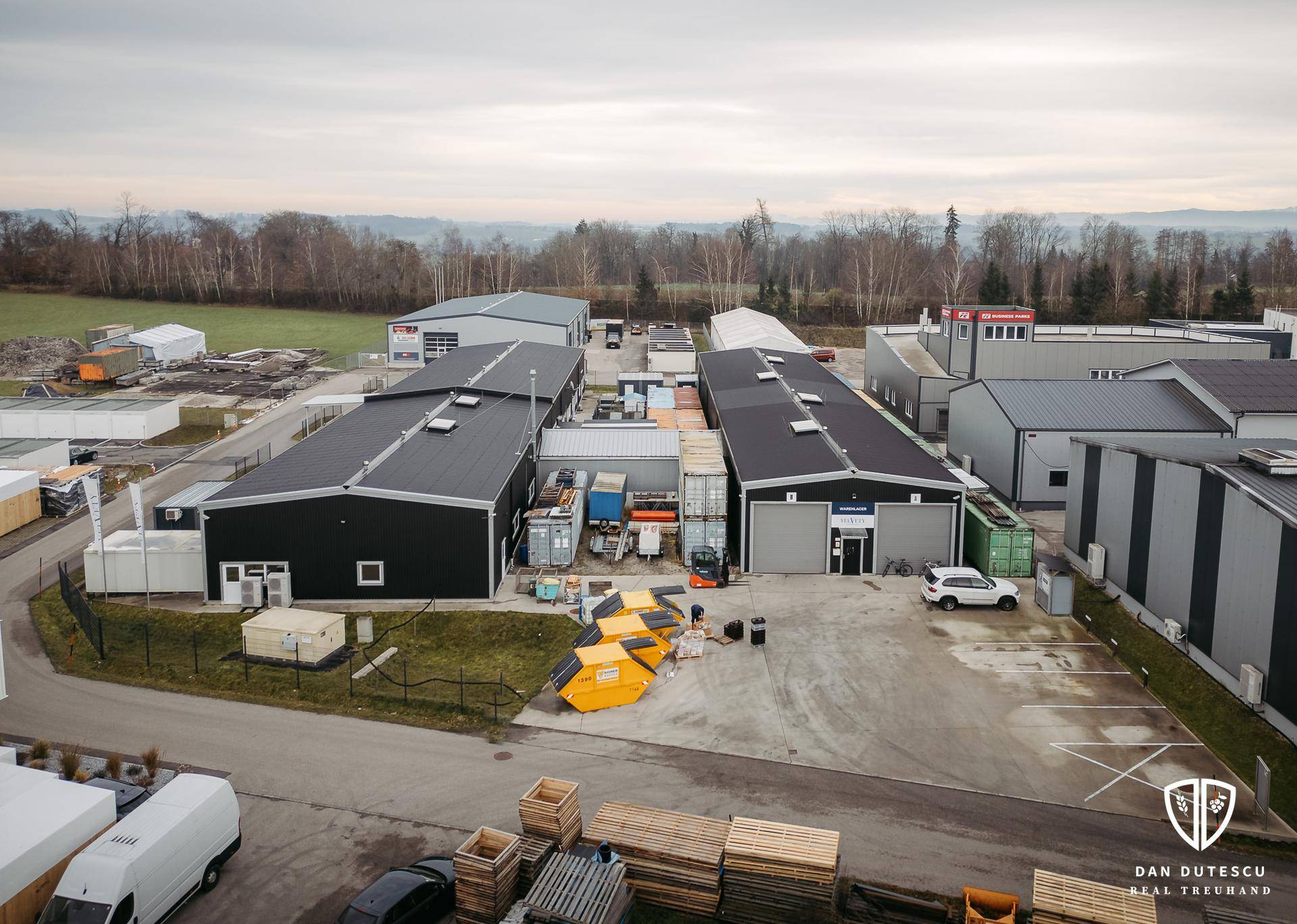 Übersichtsaufnahme des Gewerbeparks mit mehreren Hallen, Freiflächen und umliegender Naturlandschaft.