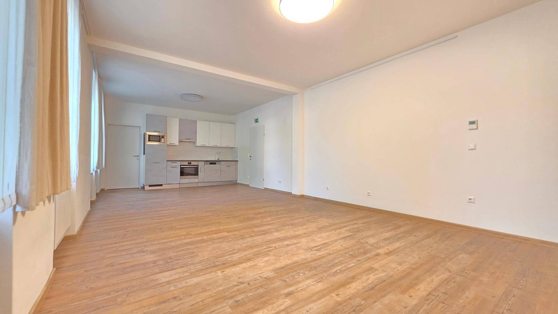 Heller, offener Wohn- und Küchenbereich mit Laminatboden und mehreren Fenstern, ideal für geselliges Beisammensein.