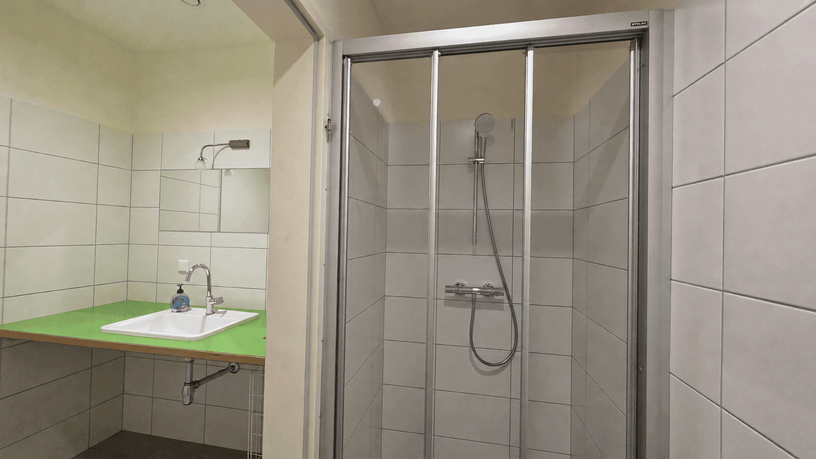 Badezimmer mit Duschkabine, Waschbecken und hellen Fliesen an den Wänden, funktional und sauber.