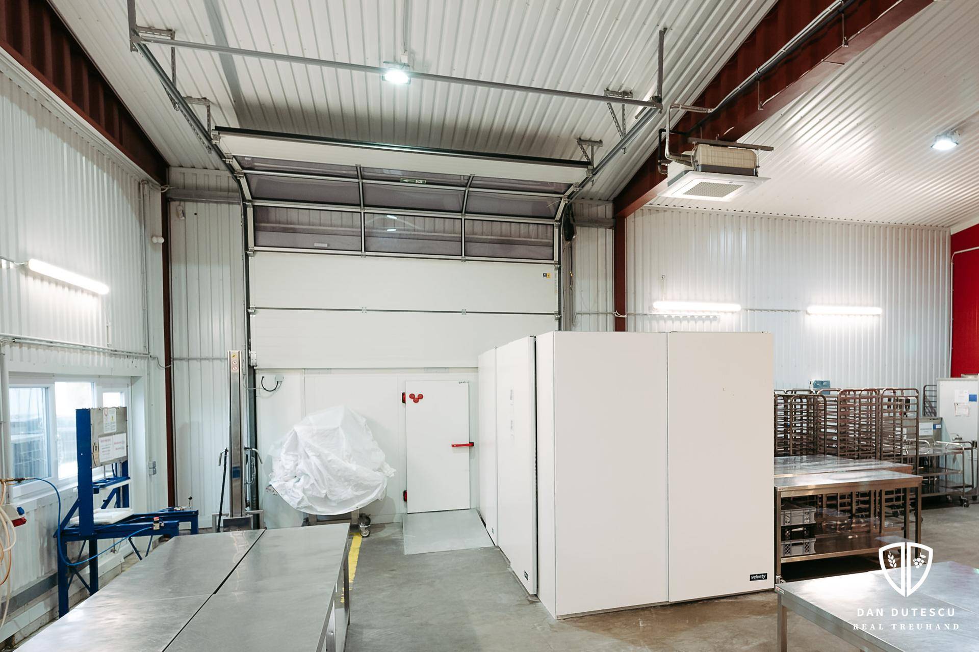 Industrielle Halle mit großem Rolltor, Edelstahltischen und hohen Decken, ideal für Produktion oder Lagerung.